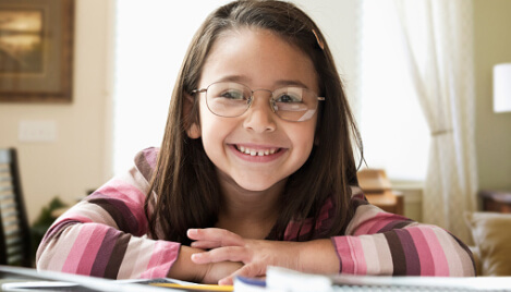 Young girl with eye glasses smiling while doing homework